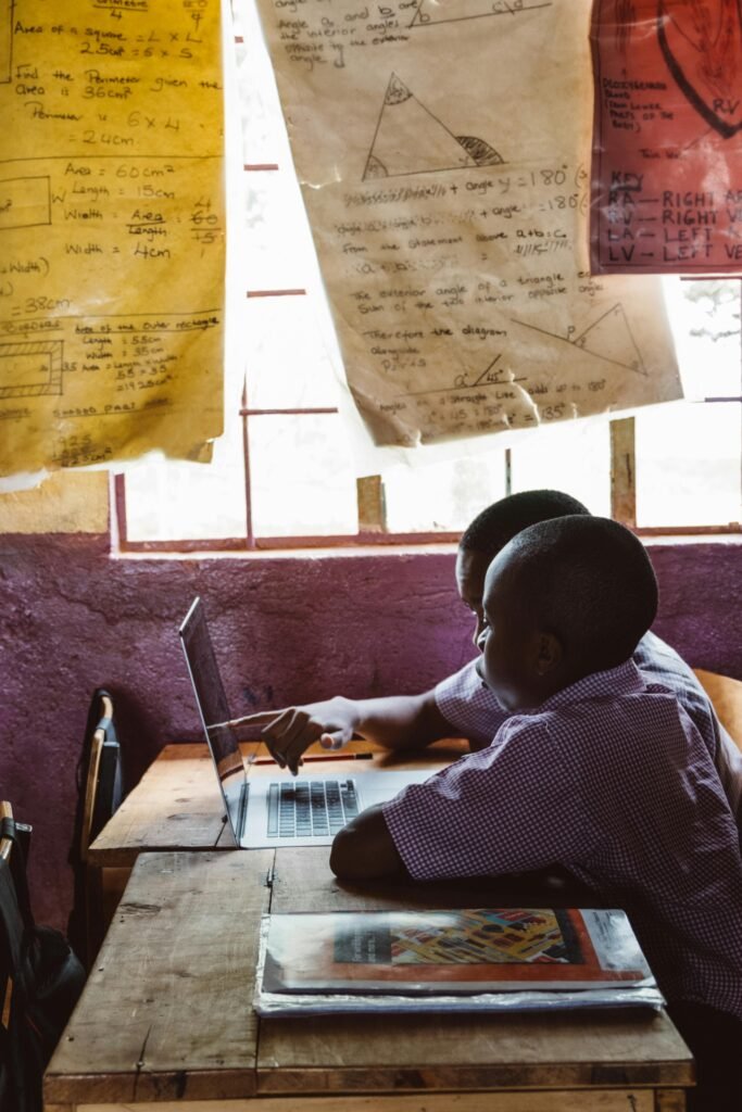 Two boys collaborate on a laptop together in a classroom setting under natural light.